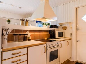 Une cuisine équipée d’une cuisinière, d’un four à micro-ondes et d’un luminaire au plafond. On y trouve des placards, une machine à café et des ustensiles de cuisine sur le plan de travail.