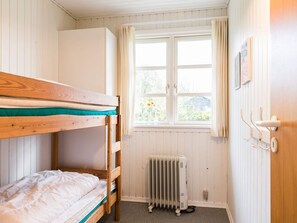Une chambre avec un lit superposé, un radiateur et une fenêtre avec des rideaux.