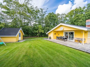 Un bĂątiment jaune dotĂ© dâune terrasse, dâun petit abri de jardin et dâune pelouse bien entretenue.