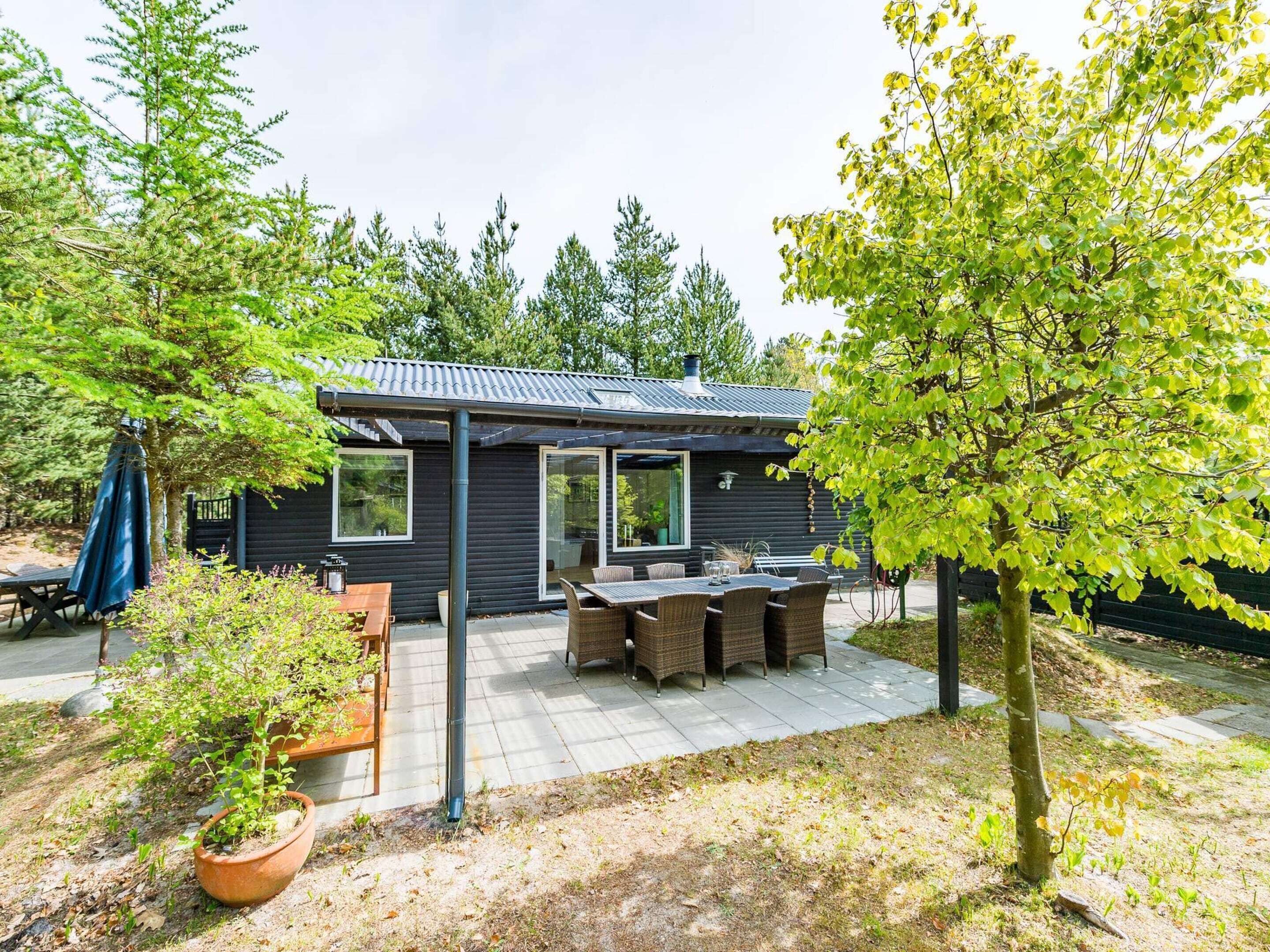 Eine moderne Holzhütte mit Terrasse, großen Fenstern und Sitzgelegenheit im Freien.