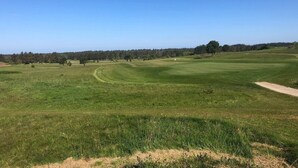 A golf course with a clear sky, a flag on the green, and a forest in the background. - 2 Person Holiday Home in Henne (Henne)