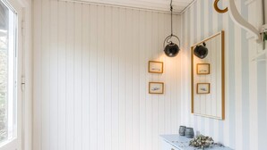 A room with white paneled walls, a light blue console table with decorative items, and framed pictures on the wall. - 2 Person Holiday Home in Henne (Henne)