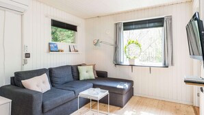 A modern living room with a grey sofa, a small white side table, and a window with a wreath decoration. - 2 Person Holiday Home in Henne (Henne)