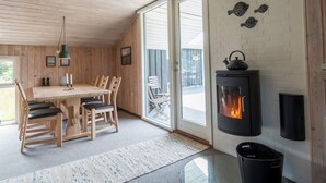 A cozy room with a wooden ceiling, a dining table with chairs, a fireplace, and a large window. - 6 Person Holiday Home in Fano (Fano)