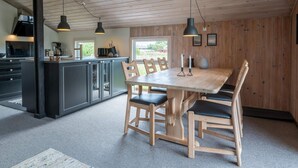 A modern kitchen with dark cabinets, a wooden dining table with chairs, pendant lights, and a view of the outdoors. - 6 Person Holiday Home in Fano (Fano)