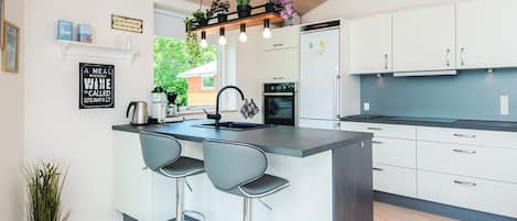 A modern kitchen with a central island, bar stools, a built-in oven, and a refrigerator.