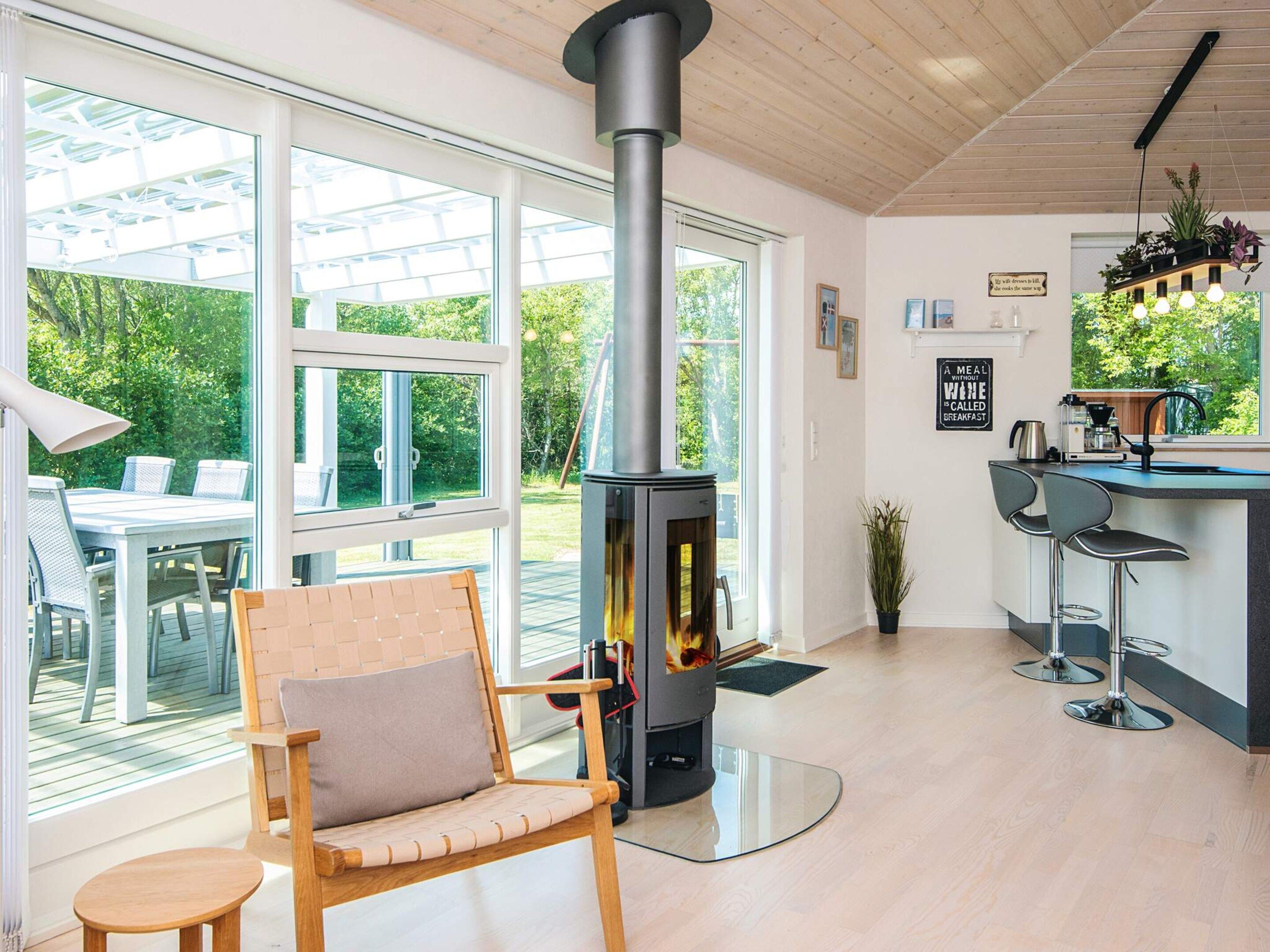 A modern kitchen with a wood-burning stove, large windows, and a dining area with outdoor seating.