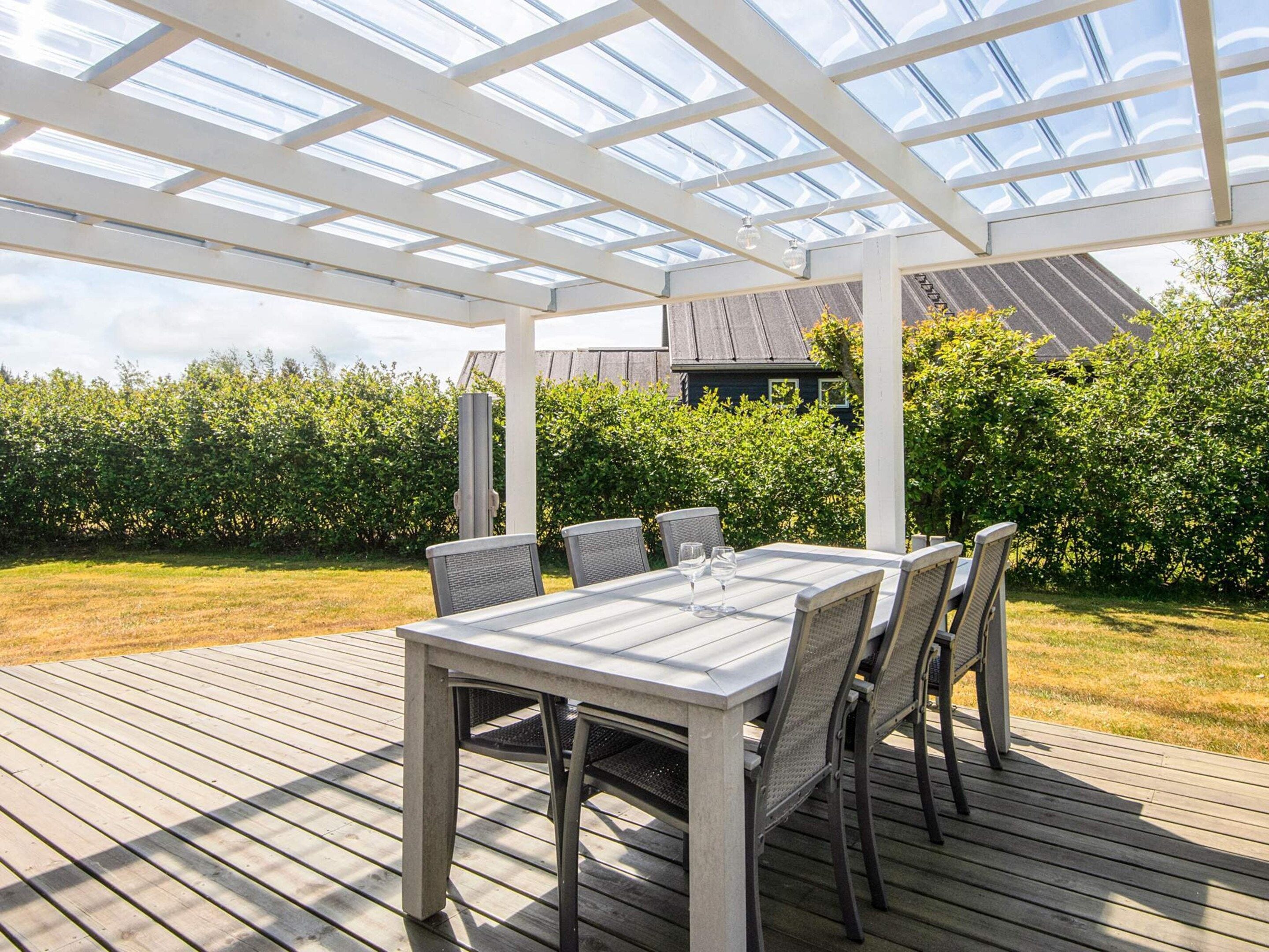 En udendørs terrasse med et glasloft, træterrasse og et bord med stole.
