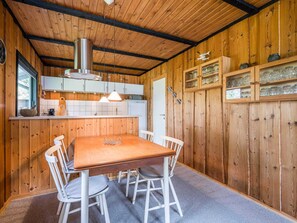 Un intérieur en bois comprenant une cuisine, une table à manger, des chaises et un meuble contenant de la verrerie.