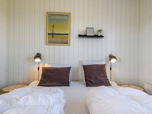 A hotel room with two beds, a wall-mounted shelf with a framed picture, and two wall-mounted lamps.