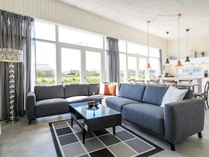 A modern living room with a grey sectional sofa, a coffee table, and a dining area with a kitchen in the background.