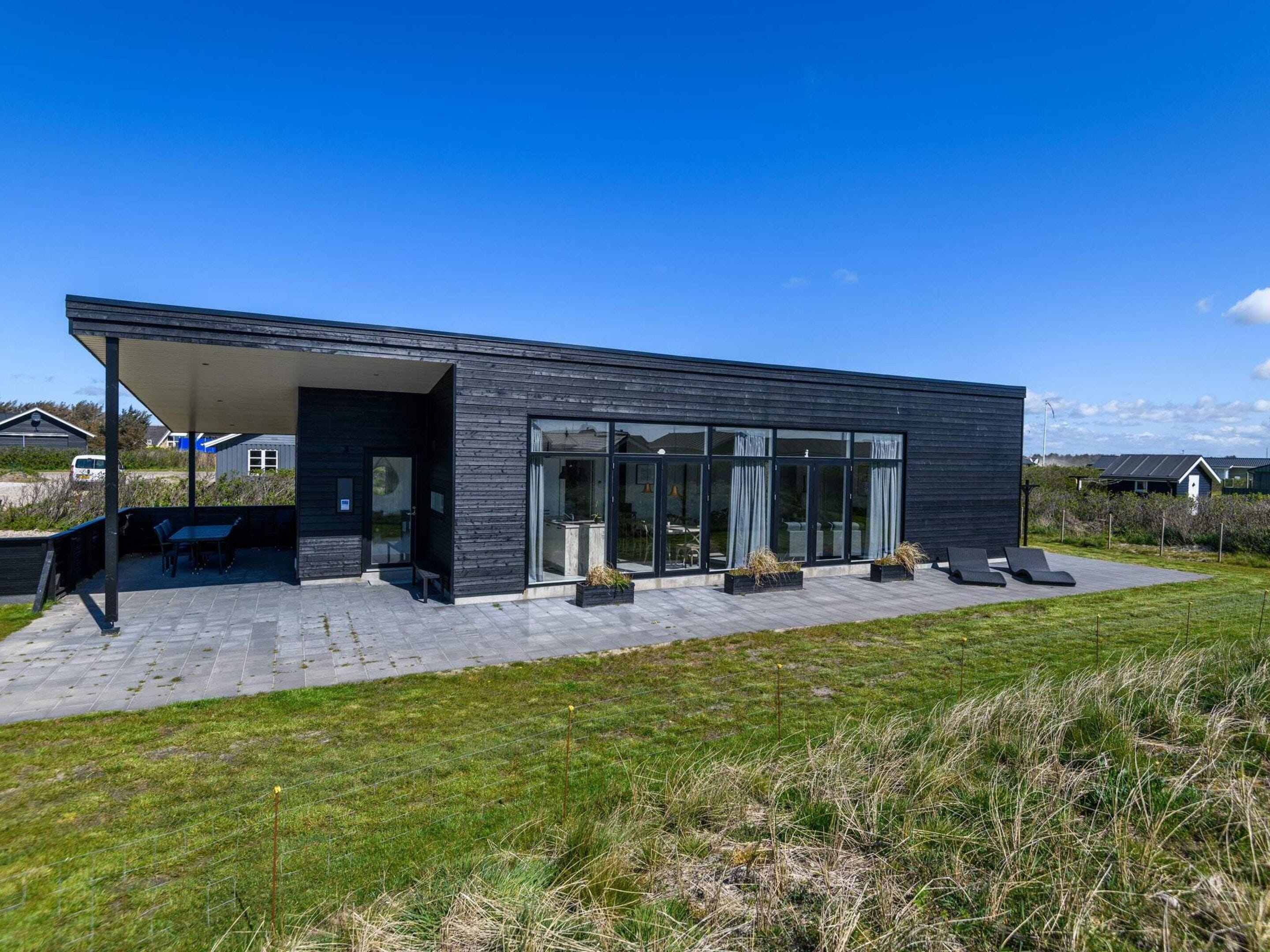 Een modern huis met een overdekt terras, grote ramen en een gazon.