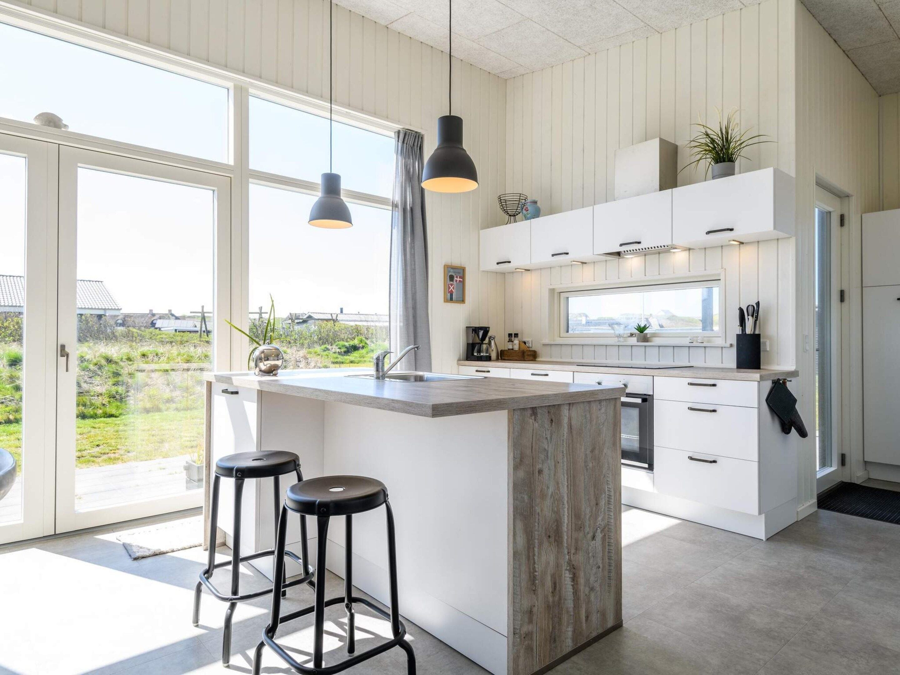 Een moderne keuken met een groot eiland, witte kasten en uitzicht op de omgeving.