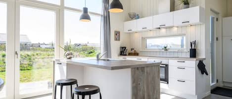 Een moderne keuken met een groot eiland, witte kasten en uitzicht op de omgeving.