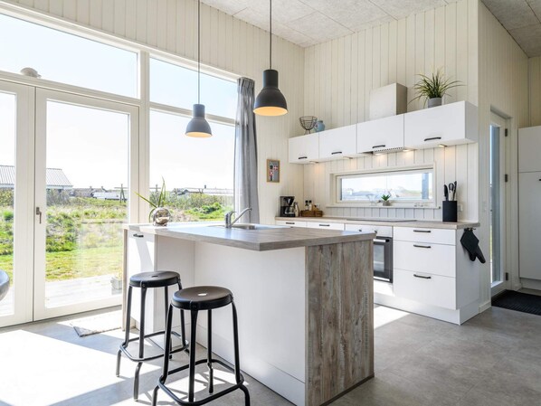 A modern kitchen with a large island, white cabinetry, and a view of the outdoors.