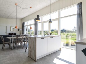 A modern kitchen with a large island, pendant lighting, and a view of the outdoors.