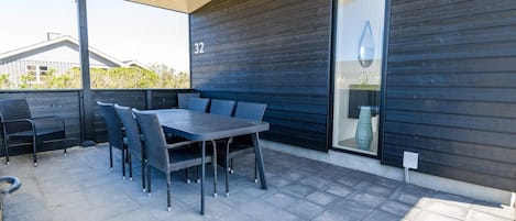 An outdoor patio with a table and chairs, a covered seating area, and a dark wooden wall with a number '32' visible.