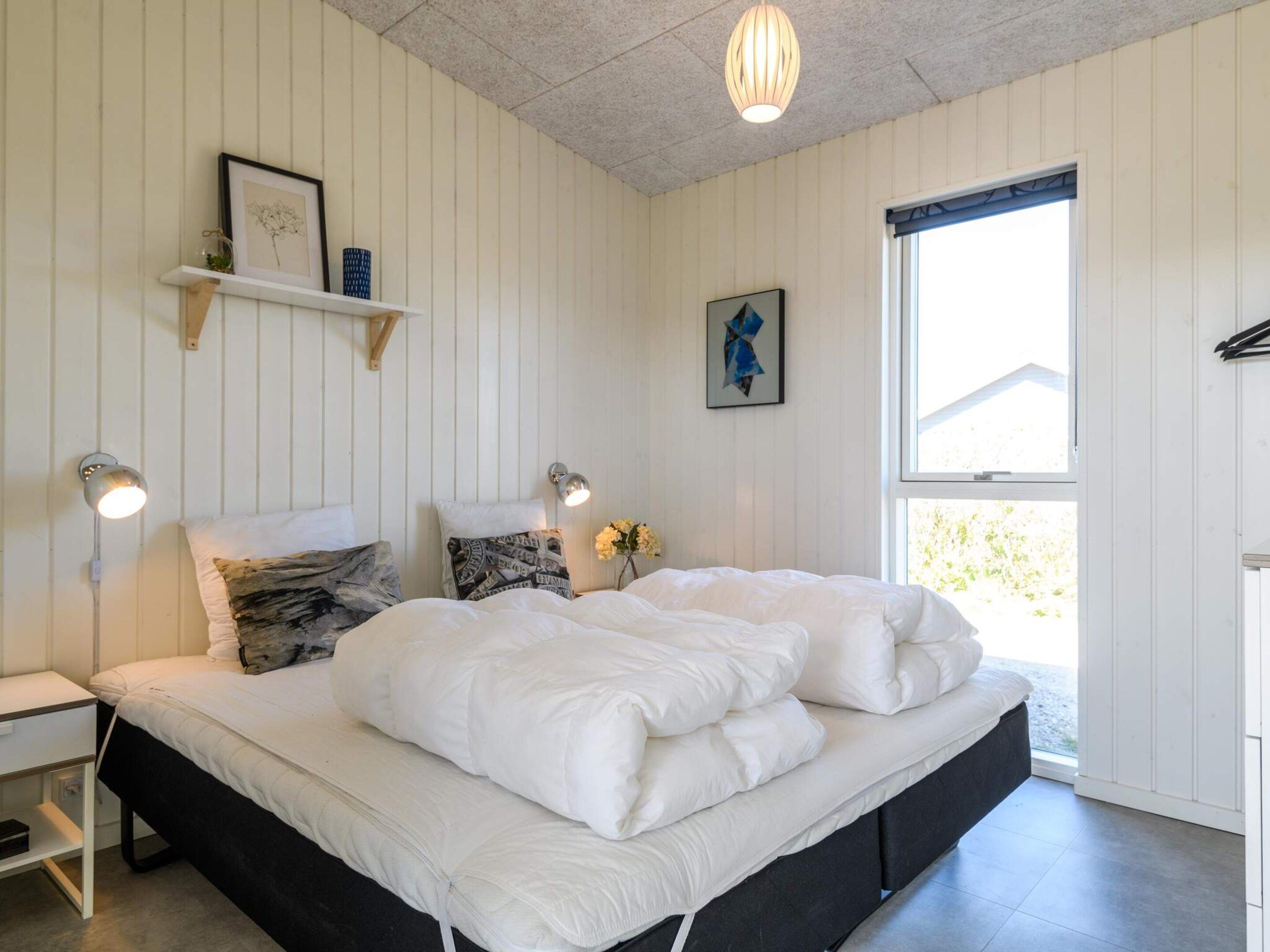 A bedroom with a bed, bedside tables, wall-mounted lamps, and a window.