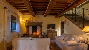 A cozy living room with a fireplace, a sofa, a television, and a staircase. - Holiday Home in Cortona (Cortona)