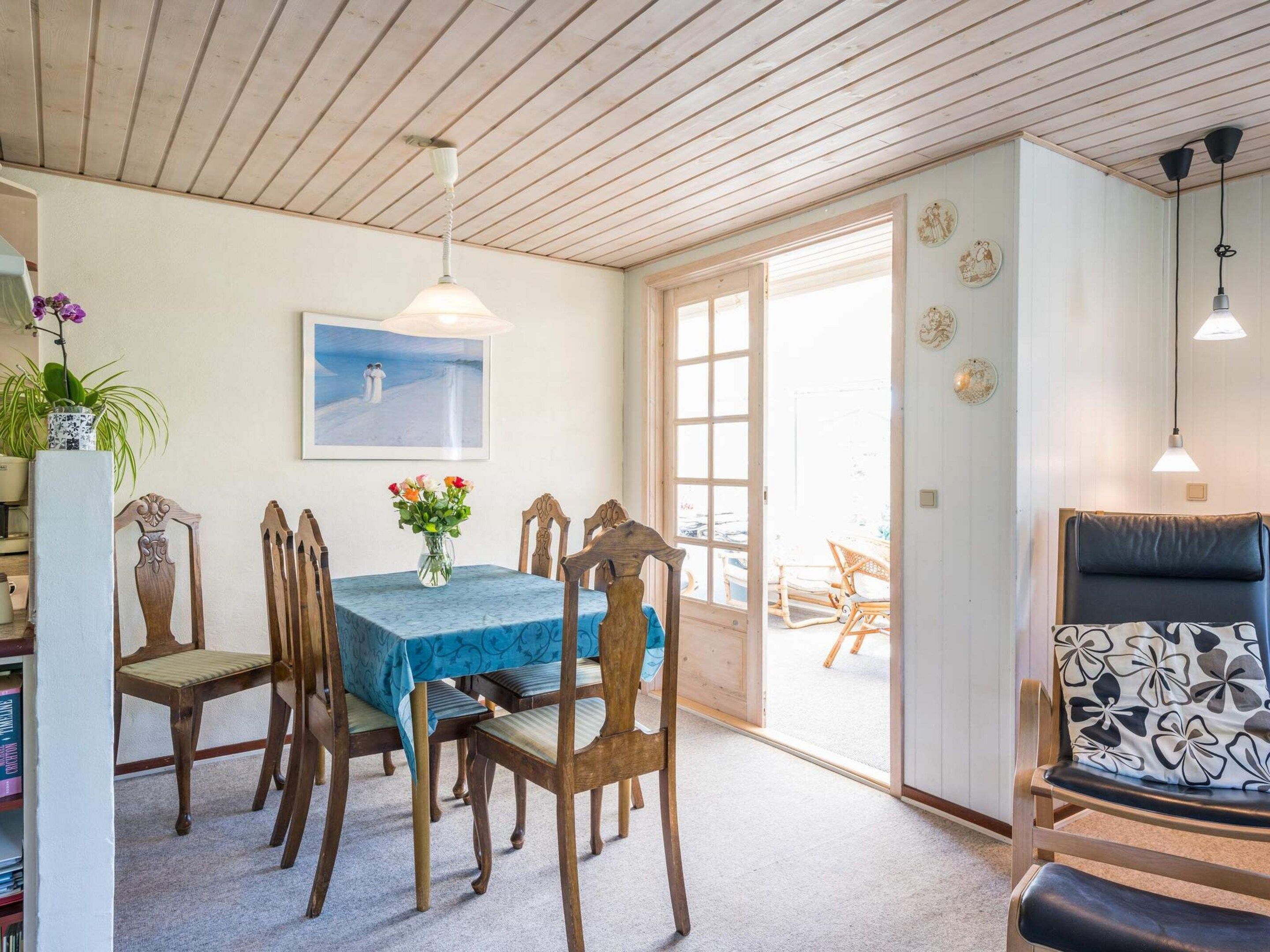 Un coin repas avec une table dressée pour quatre personnes, des chaises en bois, un vase rempli de fleurs et un tableau accroché au mur.