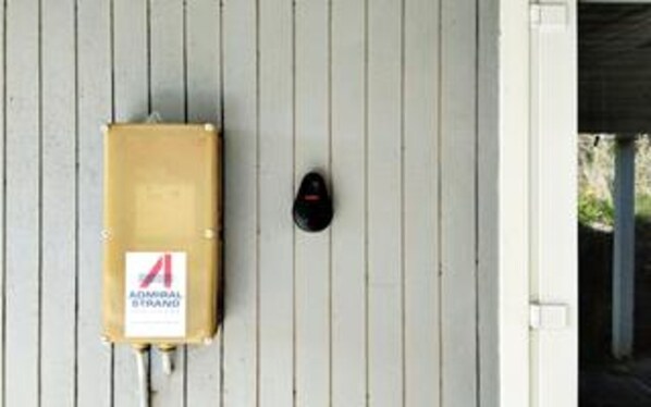 A white wall with a black security device and a brown electrical box with a label.