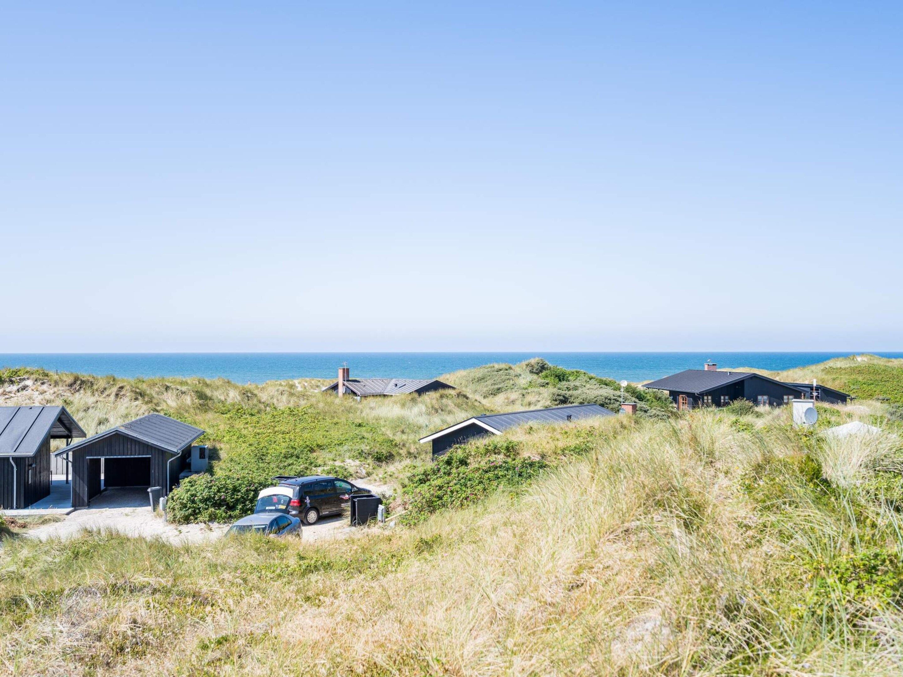 A coastal property with multiple buildings, a car, and a clear view of the sea.