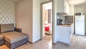 Un appartement compact doté d’une kitchenette, d’un canapé et d’un lit visible à travers une porte ouverte.