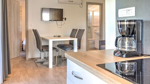 Une cuisine moderne équipée d’une machine à café, d’un téléviseur fixé au mur et d’un coin repas avec des chaises et une table.