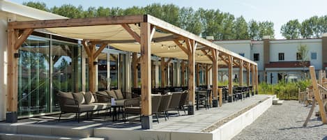 An outdoor patio area with wooden pergolas, seating arrangements, and a gravel path leading to a building.