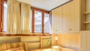 A cozy room with two beds, a sofa, and a table. There are wooden cabinets and a window with curtains. - Apartment in Cervinia With Ski Access (Valtournenche)