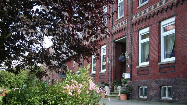 A red brick building with white window frames, a paved courtyard, and potted plants.
