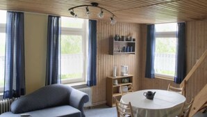 A cozy room with a wooden ceiling, a round table with chairs, a sofa, and a bookshelf.