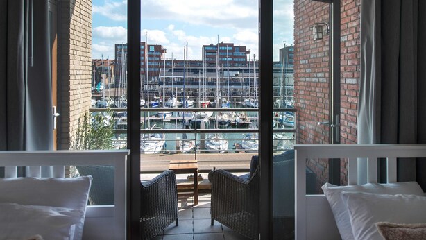 A balcony with wicker furniture, a view of a marina with boats, and a brick building in the background. - Appealing Apartment in Den Haag With Balcony (The Hague)