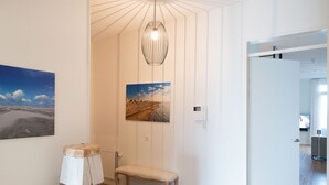 A hallway with wooden flooring, a bench, a hanging light fixture, and a painting of a beach scene. - Appealing Apartment in Den Haag With Balcony (The Hague)