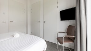 A hotel room with a bed, a chair, a TV mounted on the wall, and a door. - Brand new Luxury Villa on a Small-scale Park (Zeewolde)
