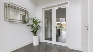A modern hallway with a potted plant, a mirror, and a door leading to a room with a bed and a lamp. - Brand new Luxury Villa on a Small-scale Park (Zeewolde)