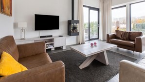A modern living room with a flat-screen TV, a fireplace, and a large window offering a view of the outdoors. - Brand new Luxury Villa on a Small-scale Park (Zeewolde)