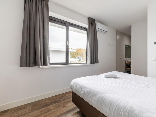 Une chambre d’hôtel avec un grand lit, une fenêtre avec des rideaux, un système de climatisation intégré, un miroir et une vue sur l’extérieur.