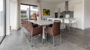 A modern kitchen with a central island, white cabinetry, and a dining area with a large table and chairs. - Brand new Luxury Villa on a Small-scale Park (Zeewolde)