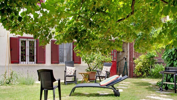 An outdoor seating area with chairs and a lounge chair, surrounded by greenery and a building with red shutters. - Rustic Moncucco Village Retreat (Moncucco Torinese)