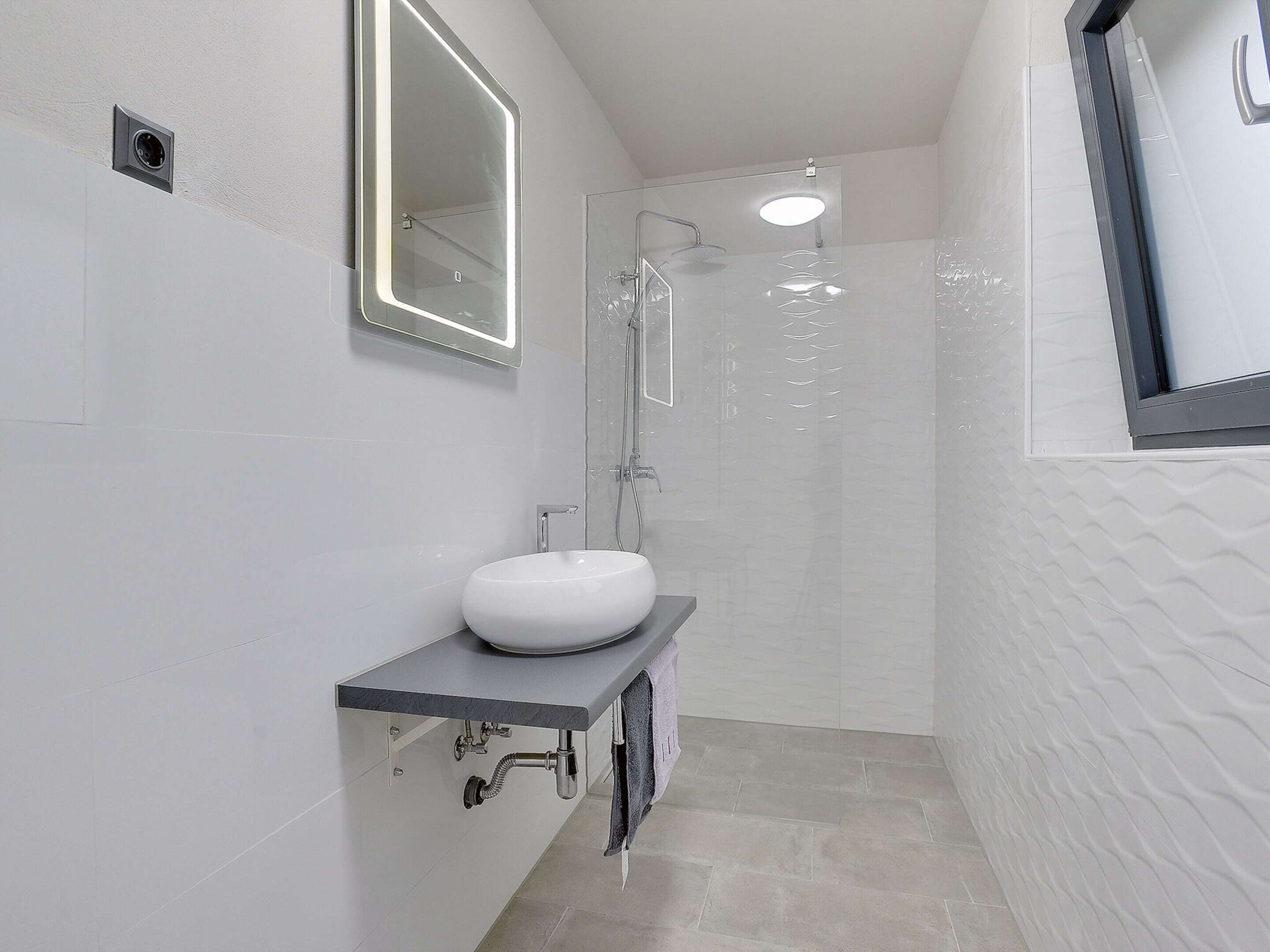 A modern bathroom with a white sink, a mirror, and a glass-enclosed shower.