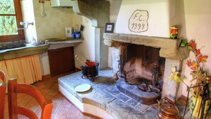 Une cuisine rustique avec une cheminée en pierre, une chaise en bois et une fenêtre donnant sur un paysage verdoyant.