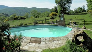 Une piscine bordée de pierres, deux chaises longues et un clocher en pierre.