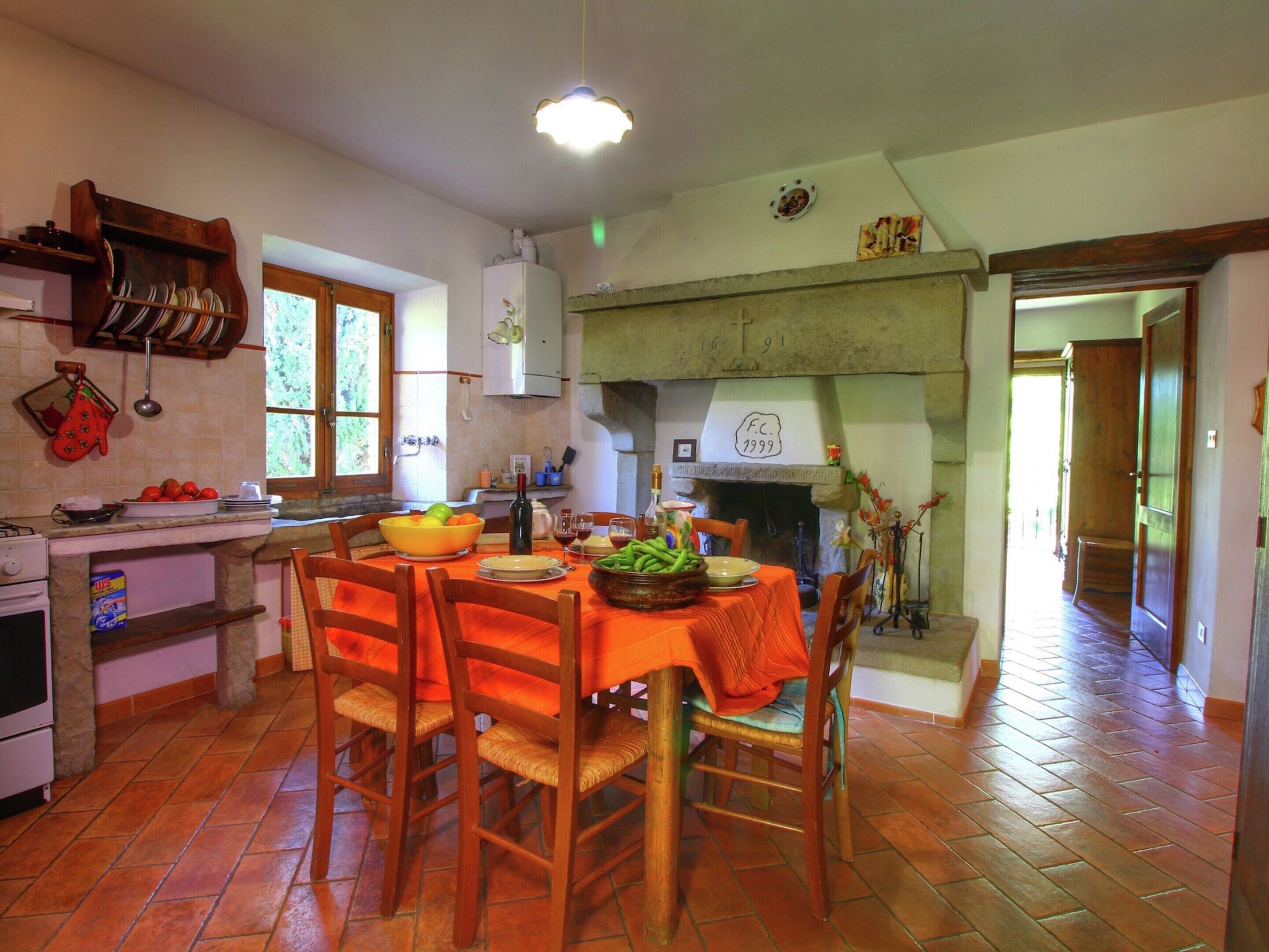 A dining area with a table set for four, a kitchen in the background, and a fireplace.