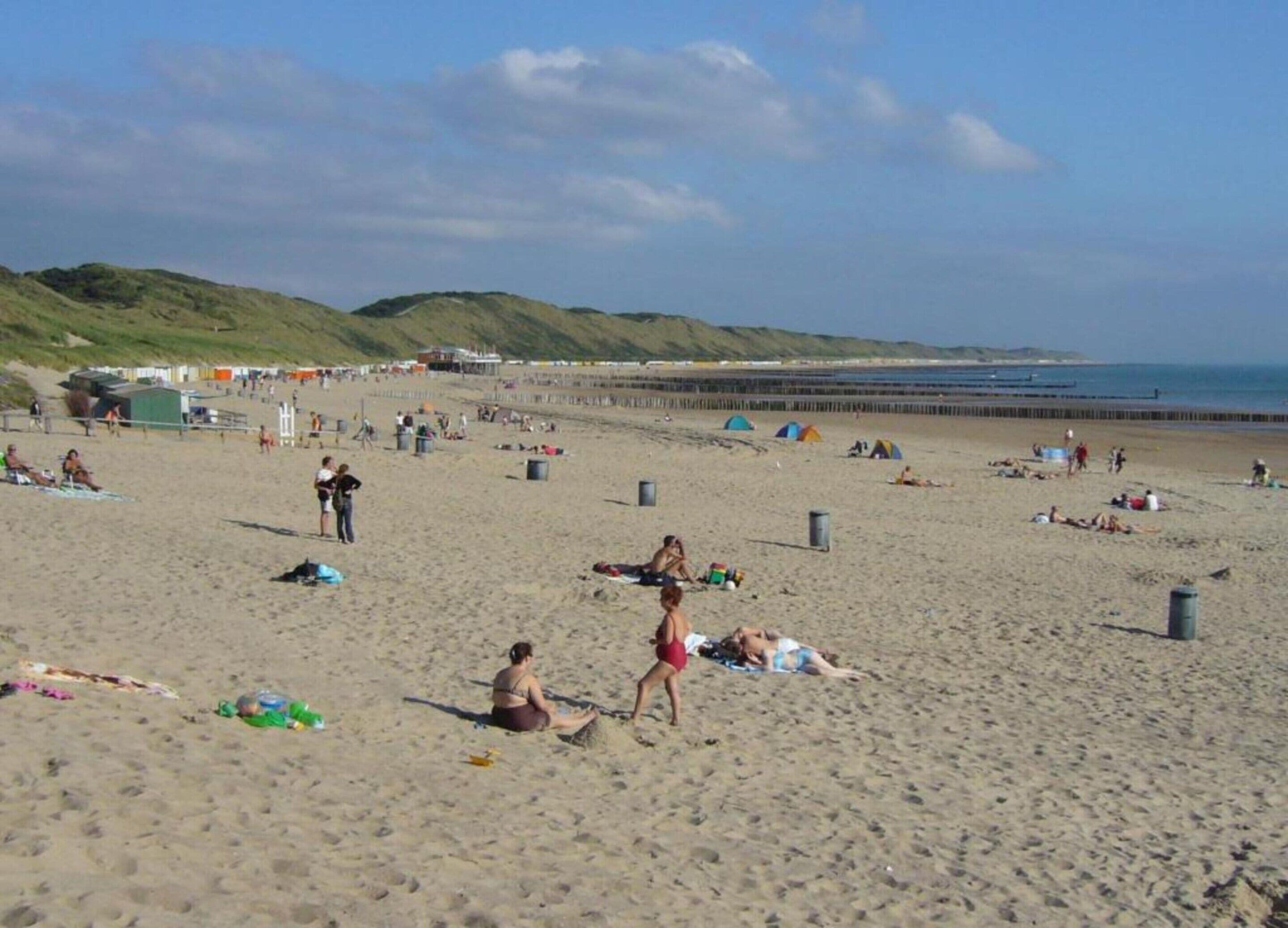 Une plage où l’on voit des gens bronzer et se promener, des tentes et, au loin, une jetée.
