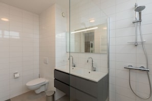 A modern bathroom with a glass shower enclosure, a white sink, and a toilet. - Stylish Beach Getaway (Zoutelande)