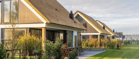 A row of modern houses with thatched roofs, large windows, and a well-maintained lawn.