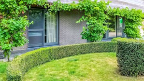 A modern building with a brick facade, large windows, and a well-maintained garden with hedges and grass. - Holiday Home in Gijverinkhove Near Plopsaland (Alveringem)