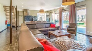 A spacious living area with a large sofa, a coffee table, and a chair. There is a kitchen in the background with a dining table and chairs. - Holiday Home in Gijverinkhove Near Plopsaland (Alveringem)