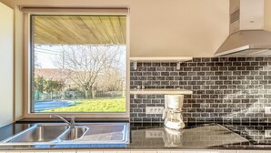 A kitchen with a window, a coffee maker, and a tiled backsplash. - Holiday Home in Gijverinkhove Near Plopsaland (Alveringem)